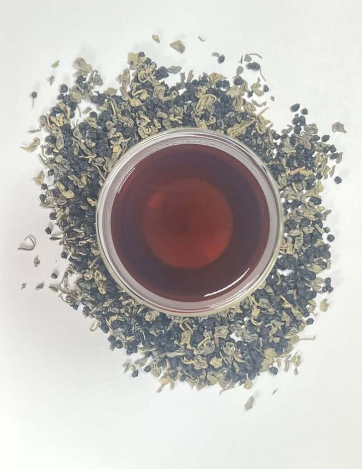 Green Tea and Elderberry Loose Leaf Herbal Tea in a glass surrounded by loose leaves.