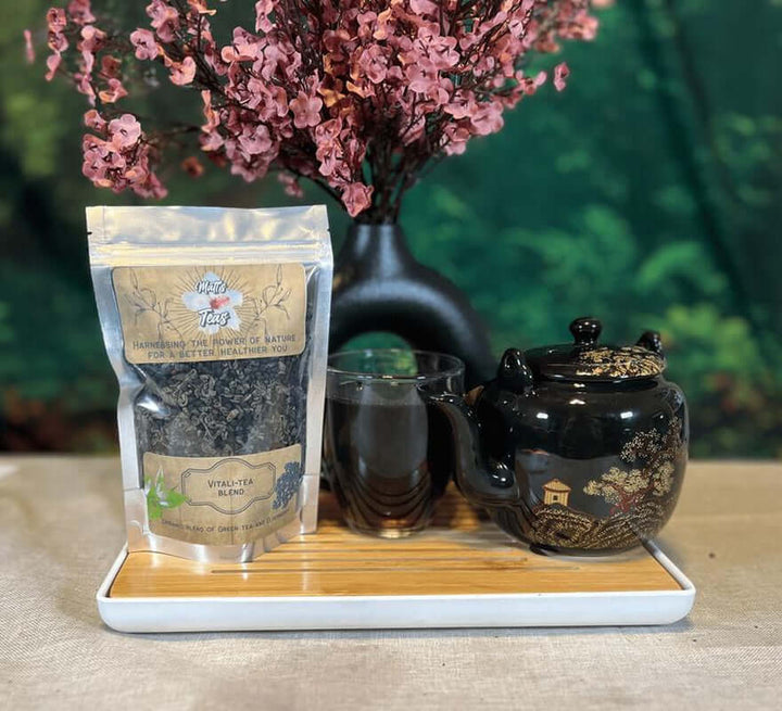 Green Tea and Elderberry Loose Leaf Herbal Tea package next to a teapot and tea cups on a wooden tray.