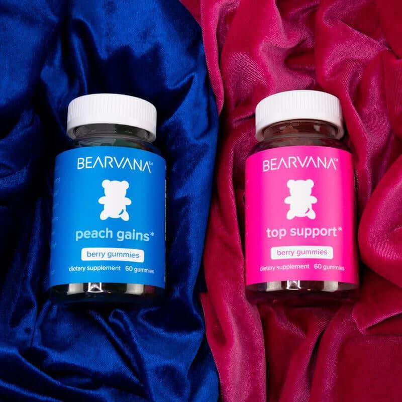 Two Bearvana gummy supplement bottles on colorful satin fabric. One blue labeled 'peach gains' and one pink 'top support'.