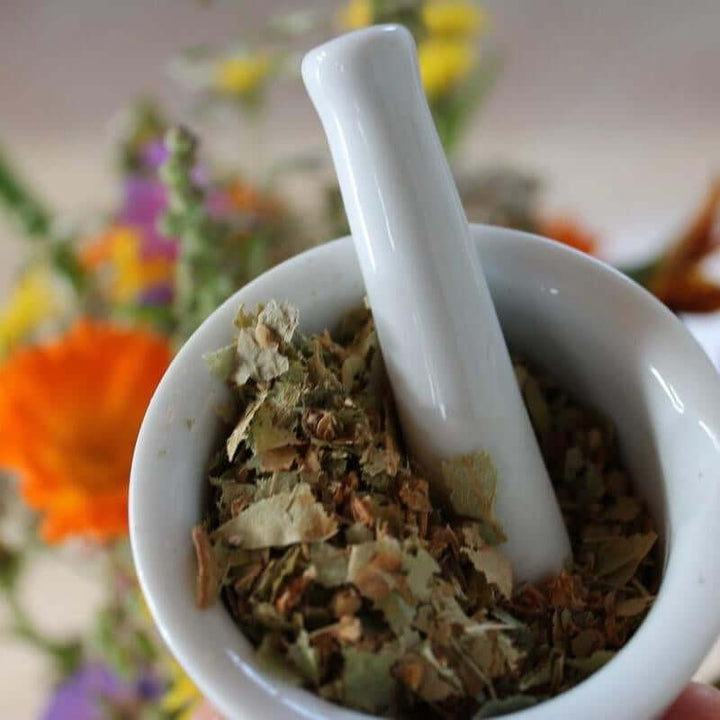 Hormone Balance Organic Herbal Tea blend in a white mortar and pestle with fresh herbs.