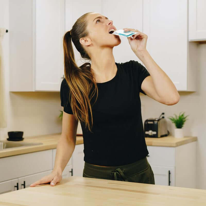 Woman consuming hydration supplements in a kitchen to stay energized and focused.