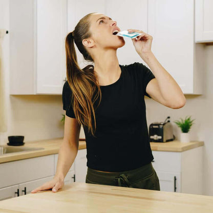 Woman consuming hydration supplements in a kitchen to stay energized and focused.